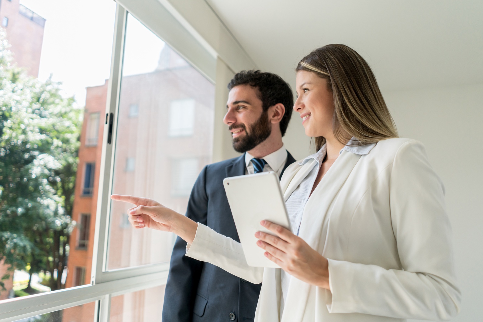 Two real estate agents looking out the window and checking real estate properties across the street.