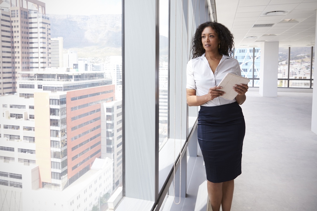A female real estate agent standing in front of a wall to ceiling window.