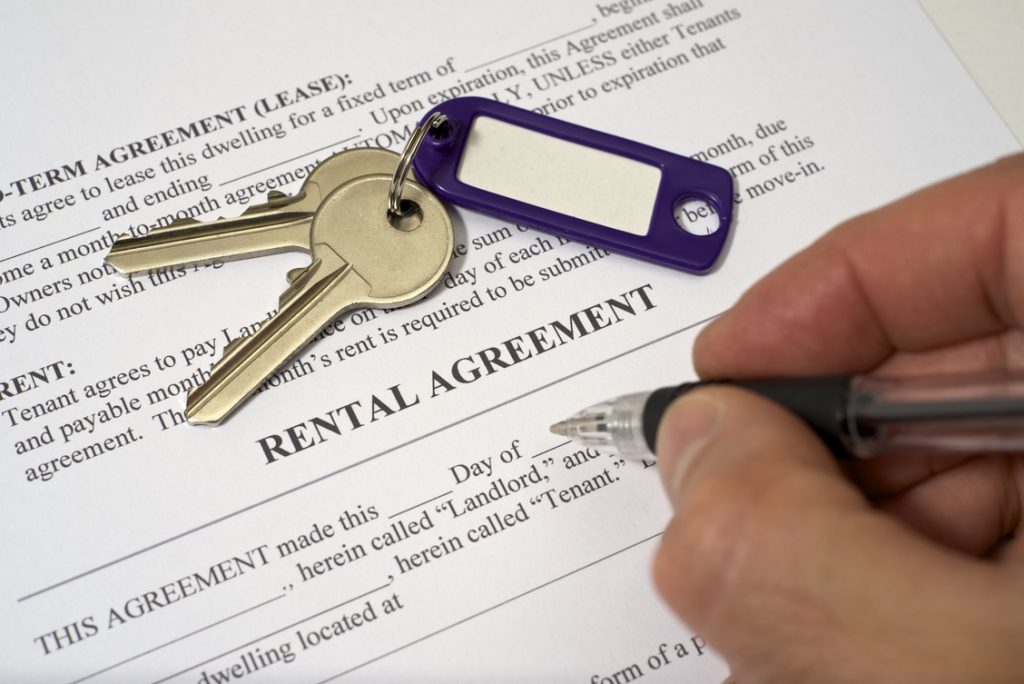 A house key and a hand signing a rental agreement