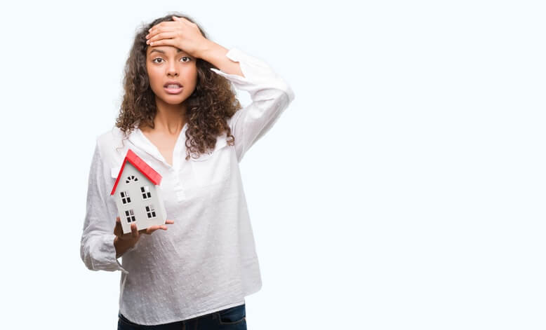 a woman holding a mini model house while other hand on her forehead