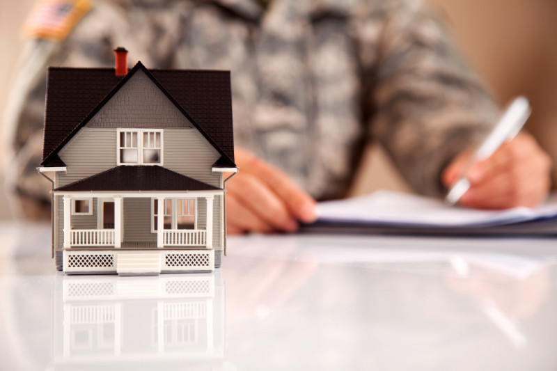 A small house model with a soldier signing papers in the background